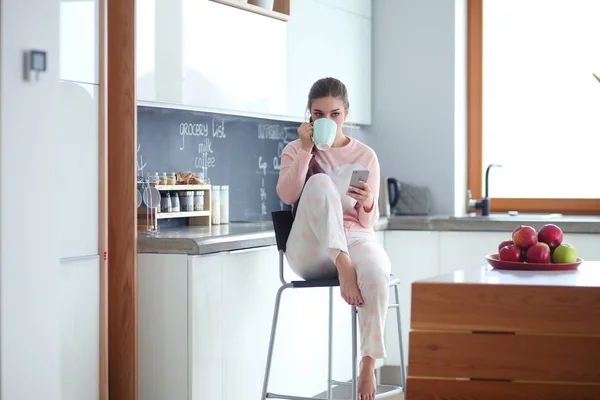 Femme utilisant un téléphone portable assis dans la cuisine moderne . — Photo