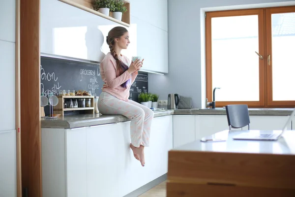 Jonge vrouw zittend op de tafel in de keuken. — Stockfoto