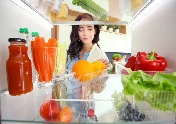 Portrait of female standing near open fridge full of healthy food, vegetables and fruits. Portrait of female — Stock Photo, Image