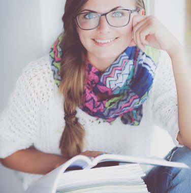 Kitapların arasında bir masada oturan genç bir kadın. Öğrenci