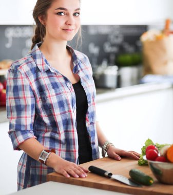 Masanın yanındaki mutfakta sebze doğrayan genç bir kadın.