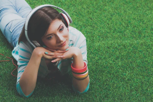 Junge Frau hört Musik und liegt auf grünem Gras — Stockfoto