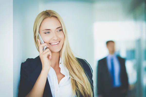 Businesswoman standing against office window talking on mobile phone — Stock Photo, Image