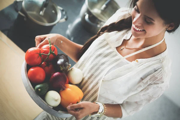 Mutfakta elinde sebzelerle gülümseyen genç bir kadın.