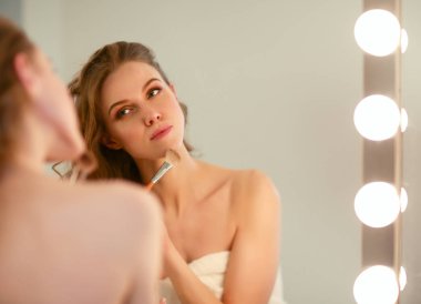 Genç bir kadın aynaya bakıyor ve makyaj yapıyor..