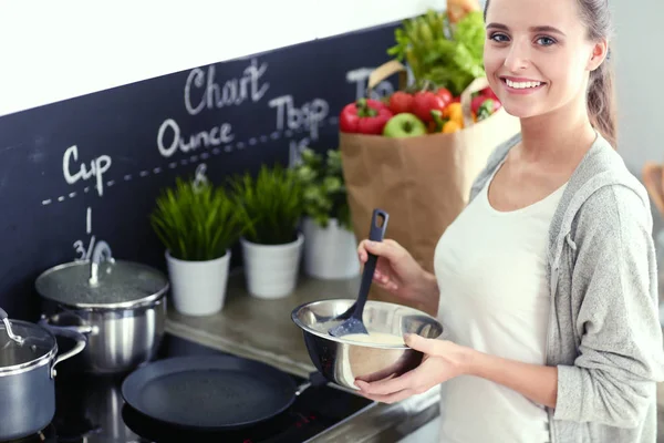 Mujer joven prepara panqueques en la cocina mientras está de pie cerca de la mesa. Mujer en la cocina. Cocinar en la cocina. — Foto de Stock