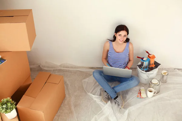 Retrato de mujer joven mientras pinta nuevo apartamento, sentado con el ordenador portátil. Mujer joven con portátil —  Fotos de Stock