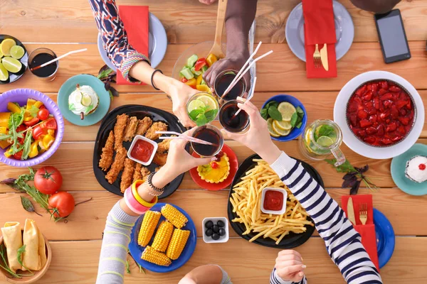 Ahşap masada otururken birlikte yemek yiyen bir grup insanın üst düzey görüntüsü. Masada yemek var. İnsanlar fast food yiyor..