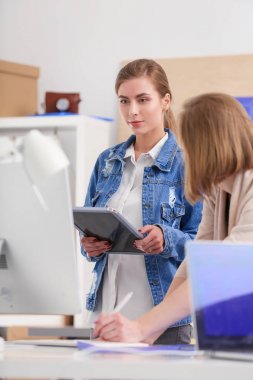 Masanın yanında duran iki genç kadın enstrüman, plan ve dizüstü bilgisayarla.