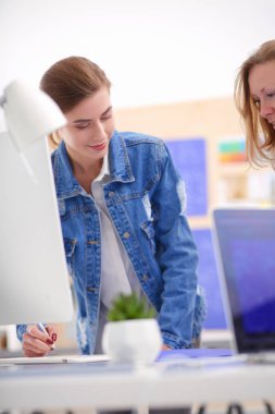 Masanın yanında duran iki genç kadın enstrüman, plan ve dizüstü bilgisayarla.