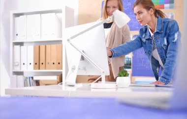 Masanın yanında duran iki genç kadın enstrüman, plan ve dizüstü bilgisayarla.