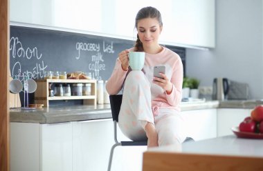 modern mutfakta otururken cep telefonu kullanan kadın.