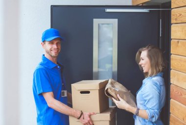 Mavi üniformalı gülümseyen kurye servis konseptine paket kutusu teslim eden teslimatçı. Mavi üniformalı gülümseyen teslimatçı.