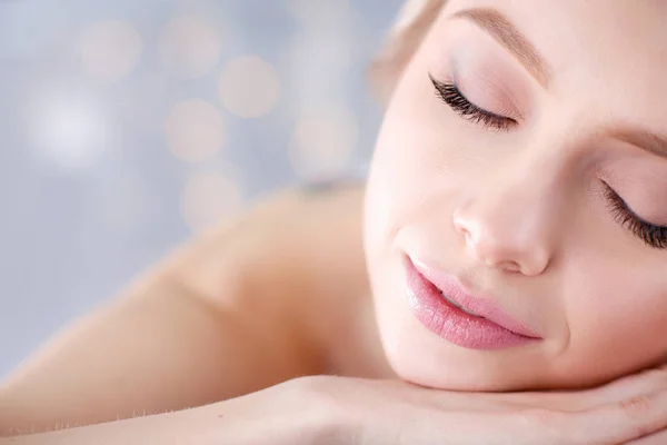 Mujer joven acostada en una mesa de masaje, relajándose con los ojos cerrados. Una mujer. Salón de spa — Foto de Stock