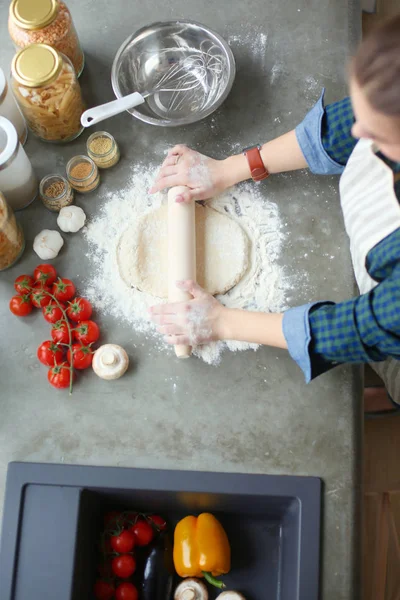 Güzel bir kadın mutfakta pasta pişiriyor. Masanın yanında duruyor..