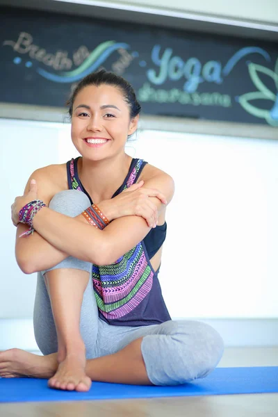 Portrait of smiling yoga woman sitting at yoga mat after workout at yoga studio. Yoga. Woman.