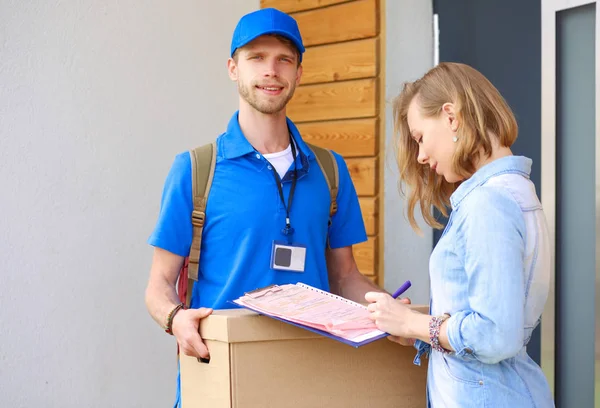 Repartidor sonriente con uniforme azul que entrega la caja de paquetes al destinatario: concepto de servicio de mensajería. Repartidor sonriente en uniforme azul — Foto de Stock