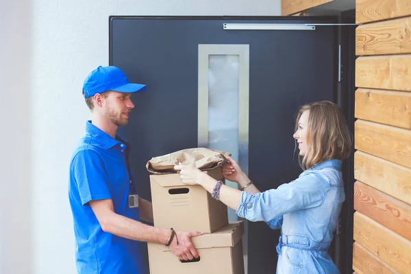 Usmívající se doručovatel v modré uniformě doručující balíček příjemci - koncept kurýrní služby. Usmívající se doručovatel v modré uniformě — Stock fotografie