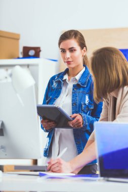 Masanın yanında duran iki genç kadın enstrüman, plan ve dizüstü bilgisayarla.