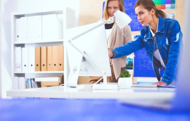 Masanın yanında duran iki genç kadın enstrüman, plan ve dizüstü bilgisayarla.