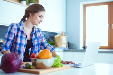 Masanın yanındaki mutfakta sebze doğrayan genç bir kadın..