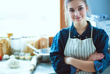 Mutfakta sobanın yanında duran genç bir kadın. .