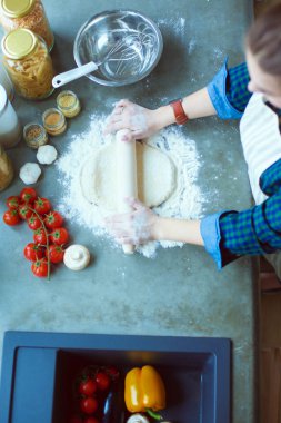 Güzel bir kadın mutfakta pasta pişiriyor. Masanın yanında duruyor..
