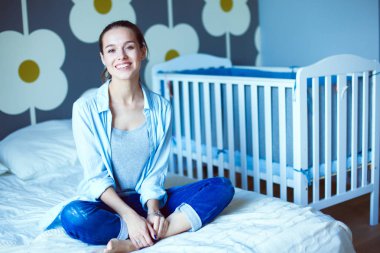 Yatakta çocuk karyolası yakın oturan bir genç bayan. Genç anne