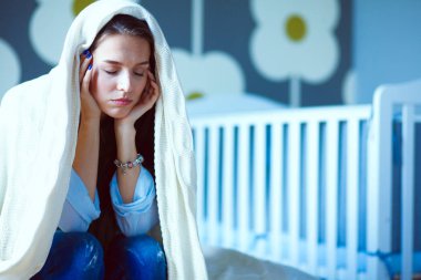 Genç çocuk karyolası yakın yatağın üstüne oturan kadın yorgun. Genç anne.