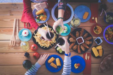 Ahşap masada otururken birlikte yemek yiyen bir grup insanın üst düzey görüntüsü. Masada yemek var. İnsanlar fast food yiyor..