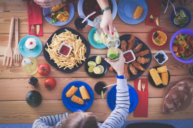 Ahşap masada otururken birlikte yemek yiyen bir grup insanın üst düzey görüntüsü. Masada yemek var. İnsanlar fast food yiyor..