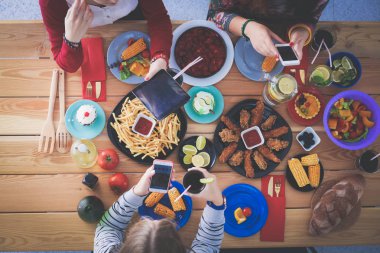 Ahşap masada otururken birlikte yemek yiyen bir grup insanın üst düzey görüntüsü. Masada yemek var. İnsanlar fast food yiyor..