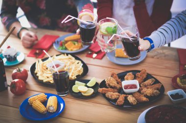 Ahşap masada otururken birlikte yemek yiyen bir grup insanın üst düzey görüntüsü. Masada yemek var. İnsanlar fast food yiyor..