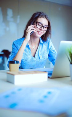 Ofis masasında oturan ve cep telefonuyla konuşan genç ve güzel bir iş kadını. İş kadını