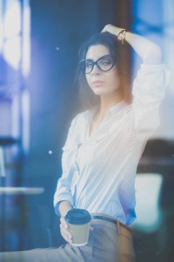 Ofis masasında dizüstü bilgisayarıyla oturan genç bir kadın. Pencereden bakıyor. Genç kadın.