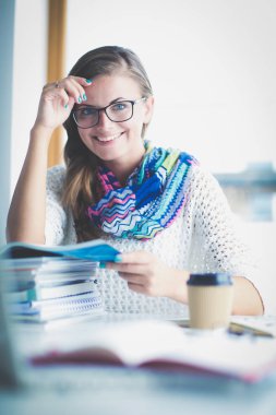 Kitapların arasında bir masada oturan genç bir kadın. Öğrenci