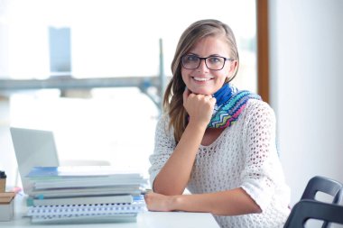 Kitapların arasında bir masada oturan genç bir kadın. Öğrenci