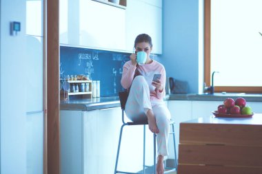 modern mutfakta otururken cep telefonu kullanan kadın.