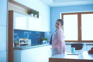 Cep telefonu ayakta modern mutfak kullanan kadın.