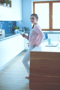 Cep telefonu ayakta modern mutfak kullanan kadın.