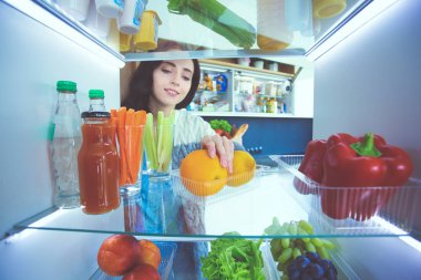 Sağlıklı yiyecek, sebze ve meyvelerle dolu açık buzdolabının yanında duran kadın portresi. Kadın portresi