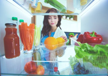 Sağlıklı yiyecek, sebze ve meyvelerle dolu açık buzdolabının yanında duran kadın portresi. Kadın portresi