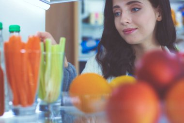 Sağlıklı yiyecek, sebze ve meyvelerle dolu açık buzdolabının yanında duran kadın portresi. Kadın portresi