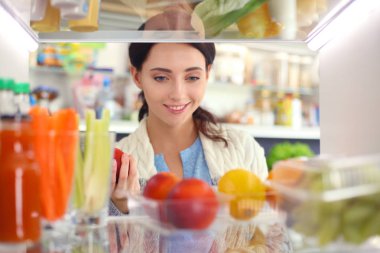 Sağlıklı yiyecek, sebze ve meyvelerle dolu açık buzdolabının yanında duran kadın portresi. Kadın portresi