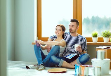 Yeni evin içini boyayan mutlu, gülümseyen genç bir çift portresi. Genç çift