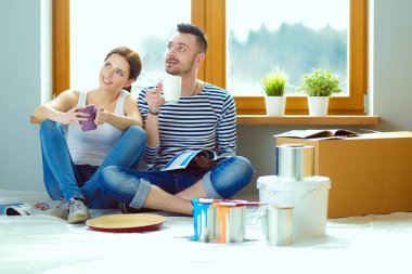 Yeni evin içini boyayan mutlu, gülümseyen genç bir çift portresi. Genç çift