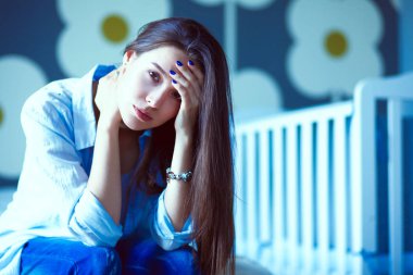 Genç çocuk karyolası yakın yatağın üstüne oturan kadın yorgun. Genç anne.