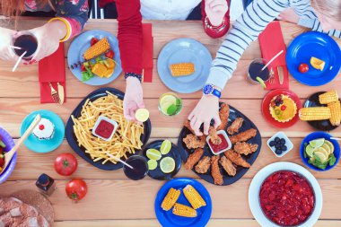 Ahşap masada otururken birlikte yemek yiyen bir grup insanın üst düzey görüntüsü. Masada yemek var. İnsanlar fast food yiyor..
