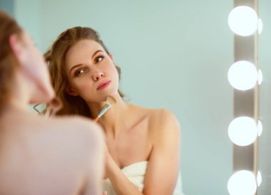 Genç bir kadın aynaya bakıyor ve makyaj yapıyor..