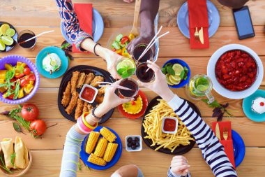 Ahşap masada otururken birlikte yemek yiyen bir grup insanın üst düzey görüntüsü. Masada yemek var. İnsanlar fast food yiyor..